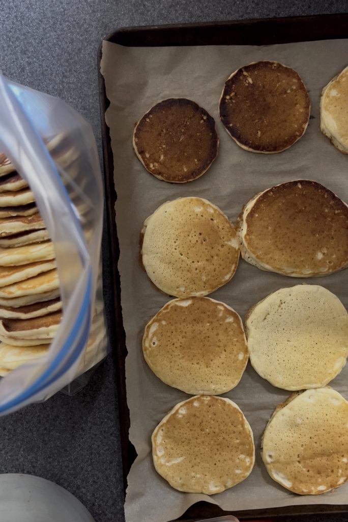 Greek yogurt pancakes cooling on a parchment-lined sheet pan beside a freezer bag