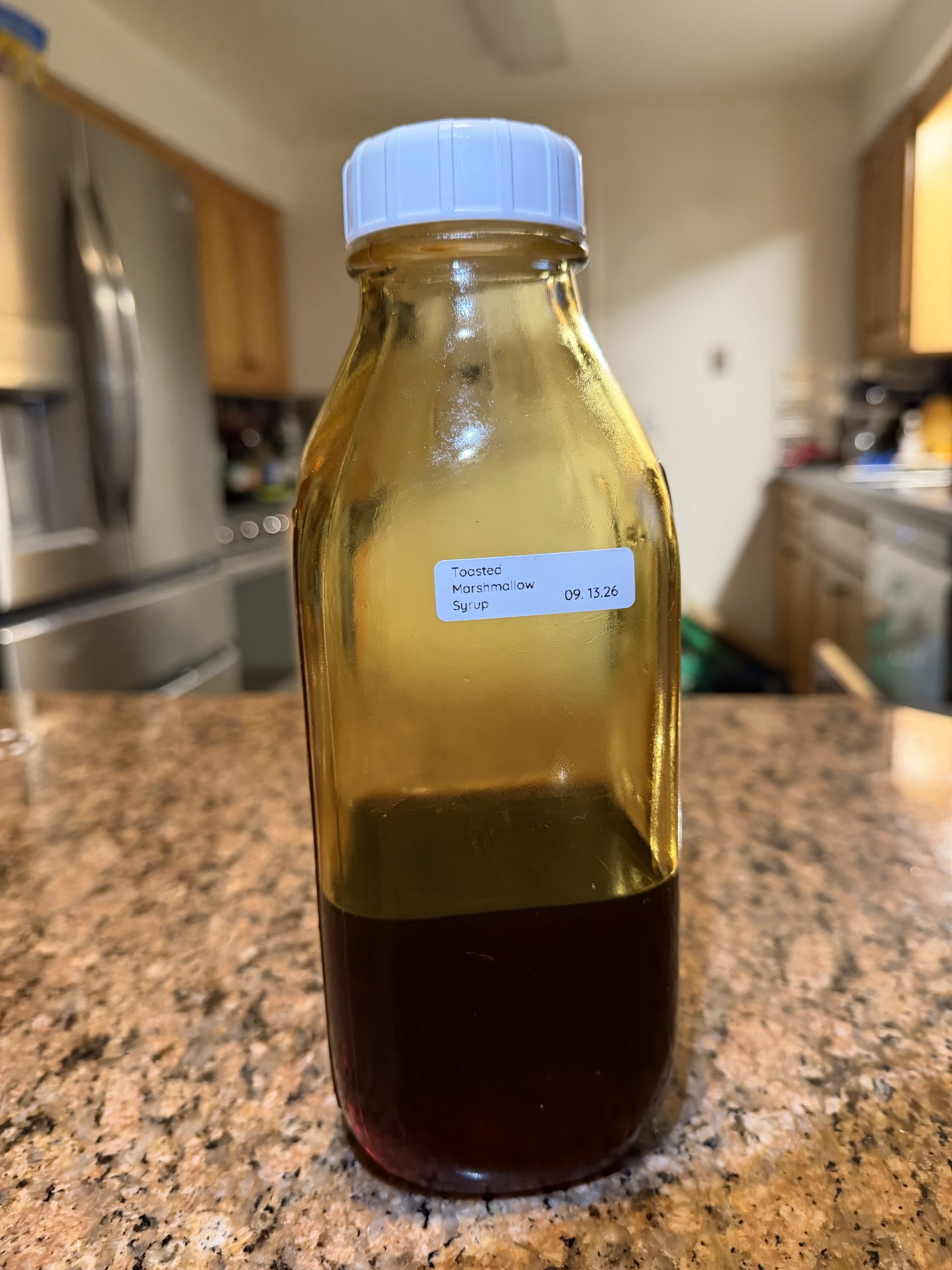 Glass bottle of homemade toasted marshmallow coffee syrup beside a small squeeze bottle.