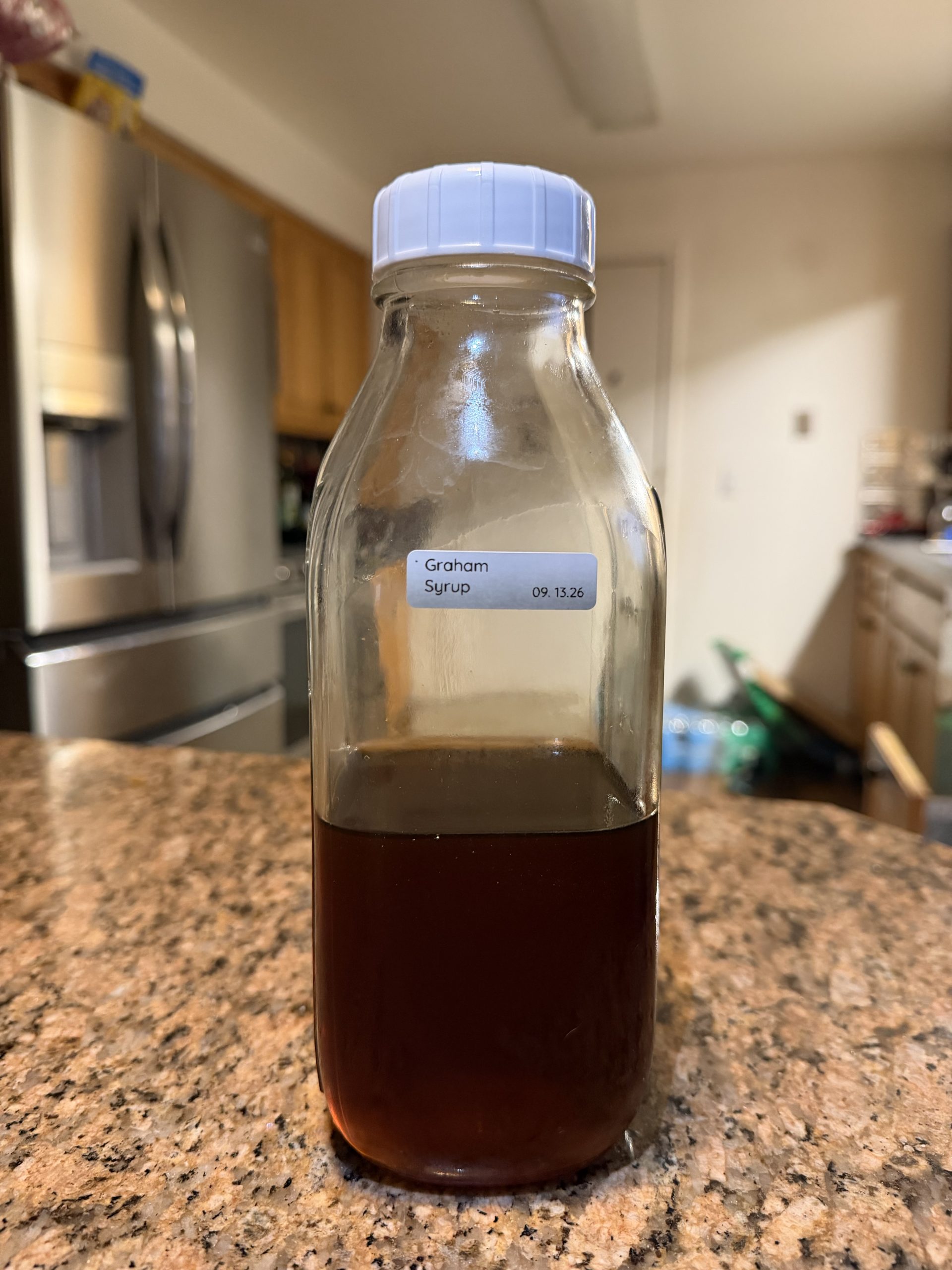 Homemade graham cracker coffee syrup in a labeled glass bottle on the kitchen counter.