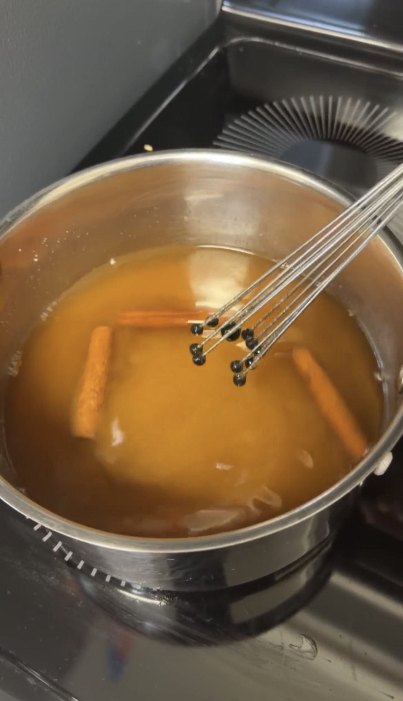 Homemade graham cracker coffee syrup simmering with cinnamon sticks in a saucepan.